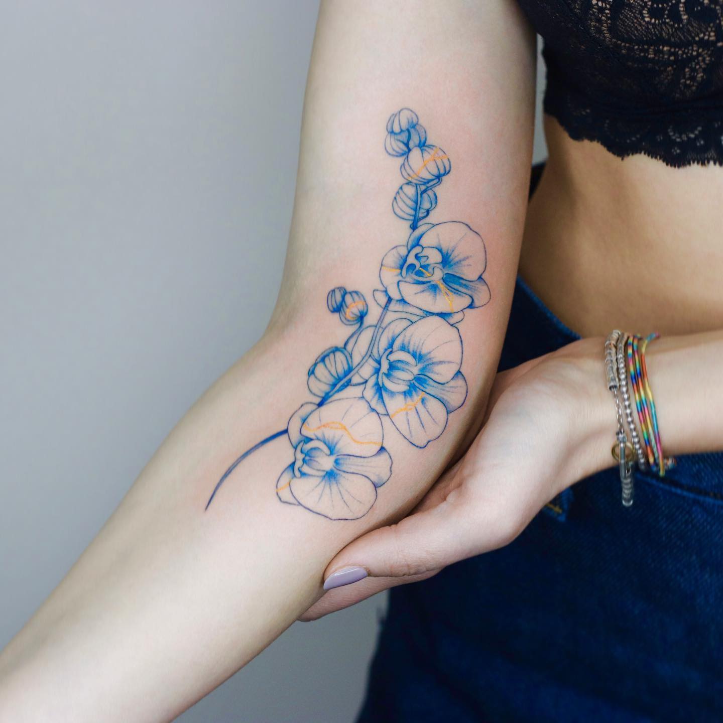 Kintsugi orchids in blue ink tattooed on the arm