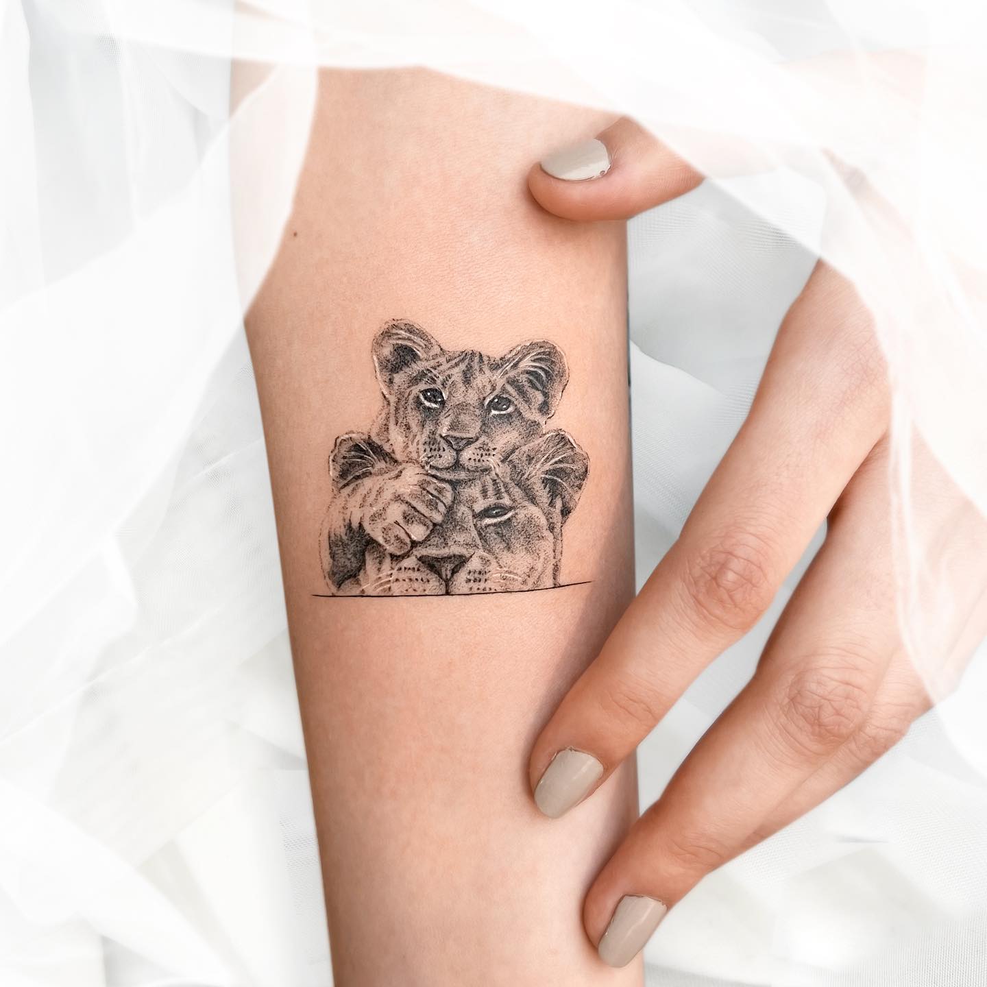 Micro-realistic lioness and lion cub tattoo on the inner forearm