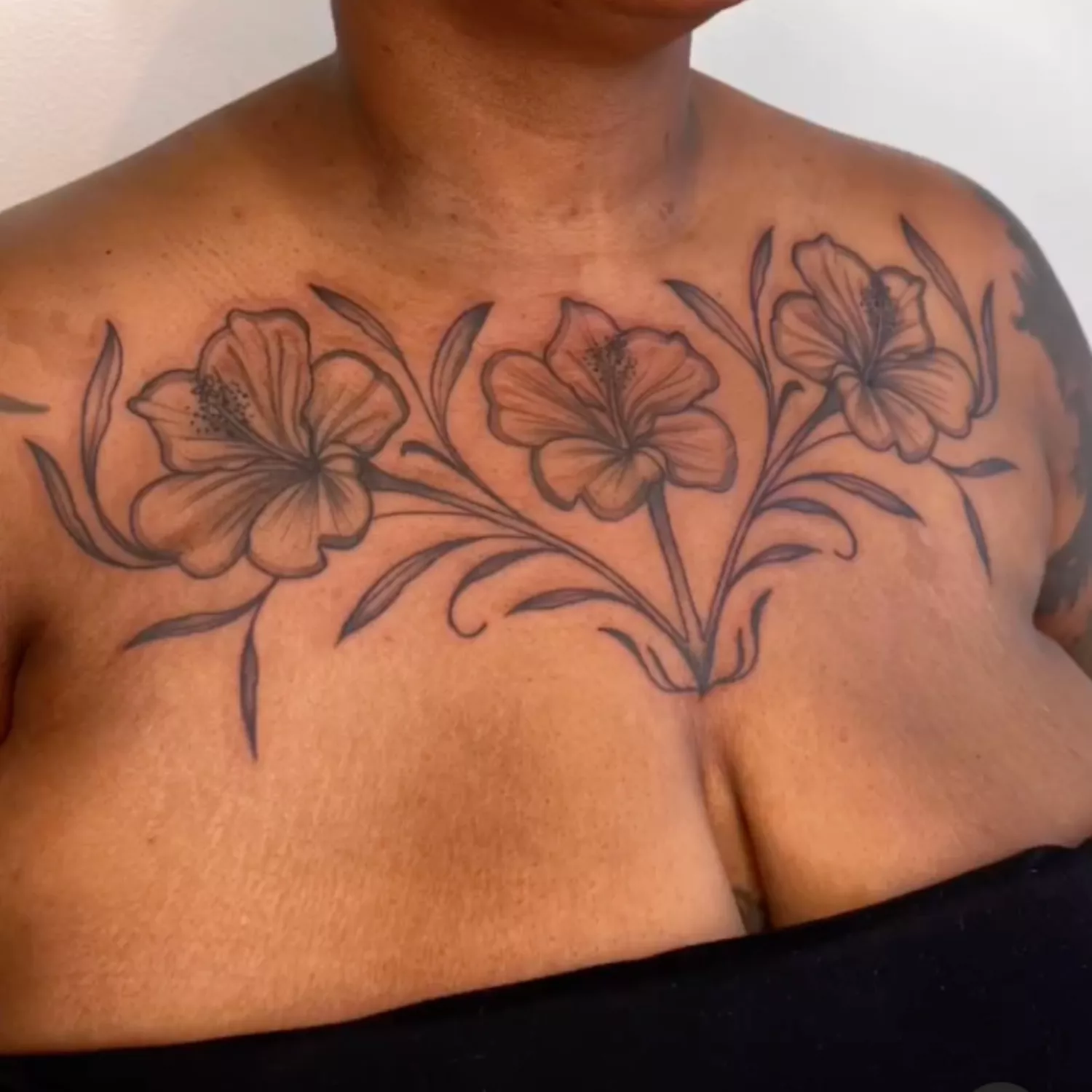 zoomed-in image of model with large statement tattoo across chest and collarbone, florals in black ink