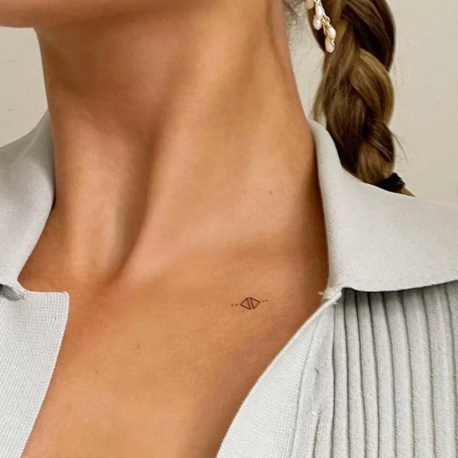 zoomed-in image of model with black ink small micro tattoo of triangles and dots on collarbone