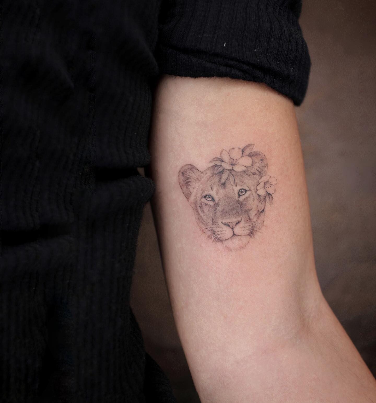 Micro-realistic lioness portrait with flowers tattooed on the inner arm