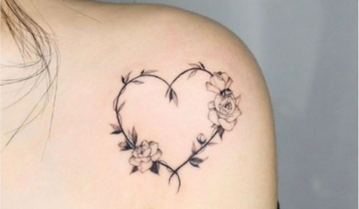 This may contain: a heart shaped tattoo with flowers on the back of her shoulder and behind it is a rose