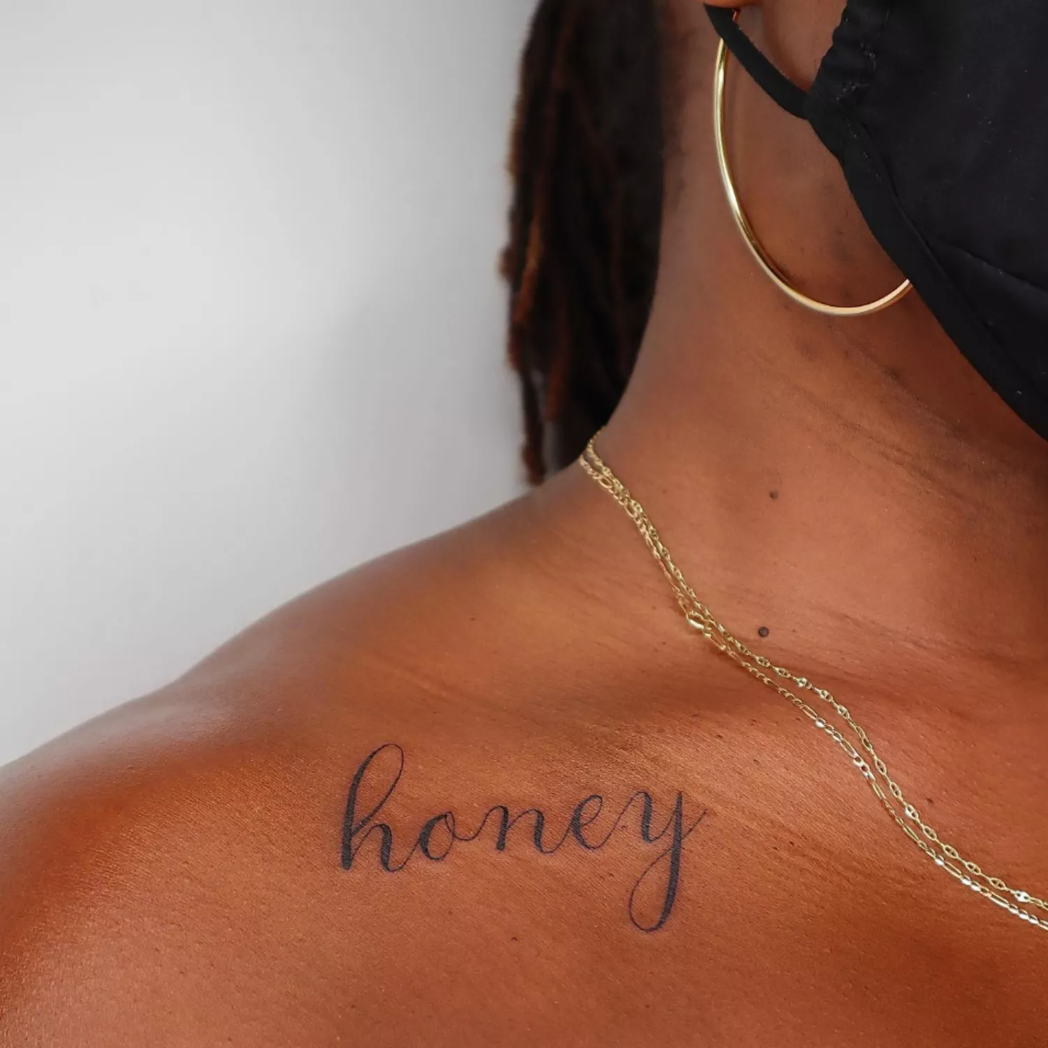 zoomed in image of model with script tattoo on collarbone that says honey in cursive