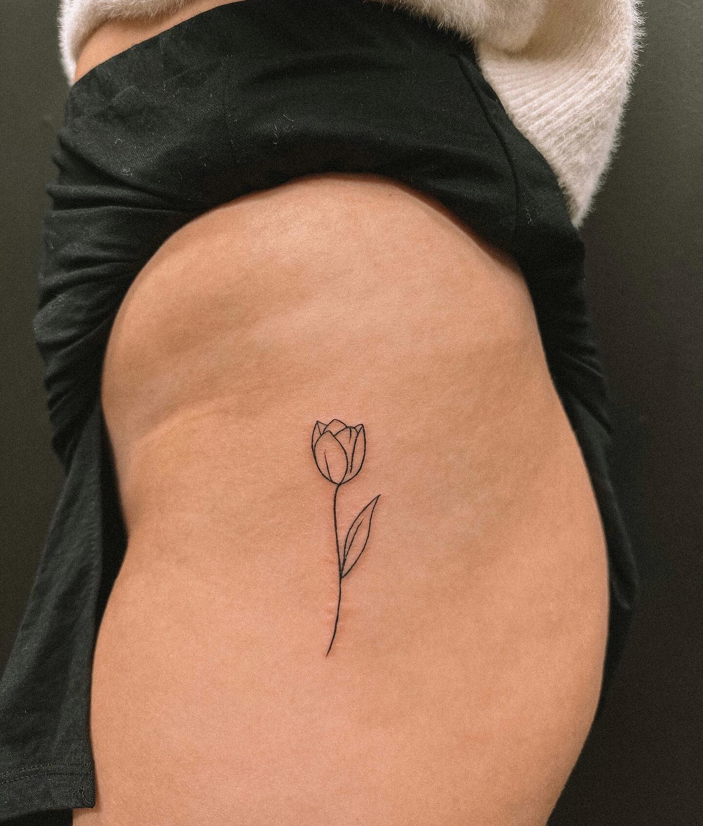 Fine line style tulip flower tattoo on the hip