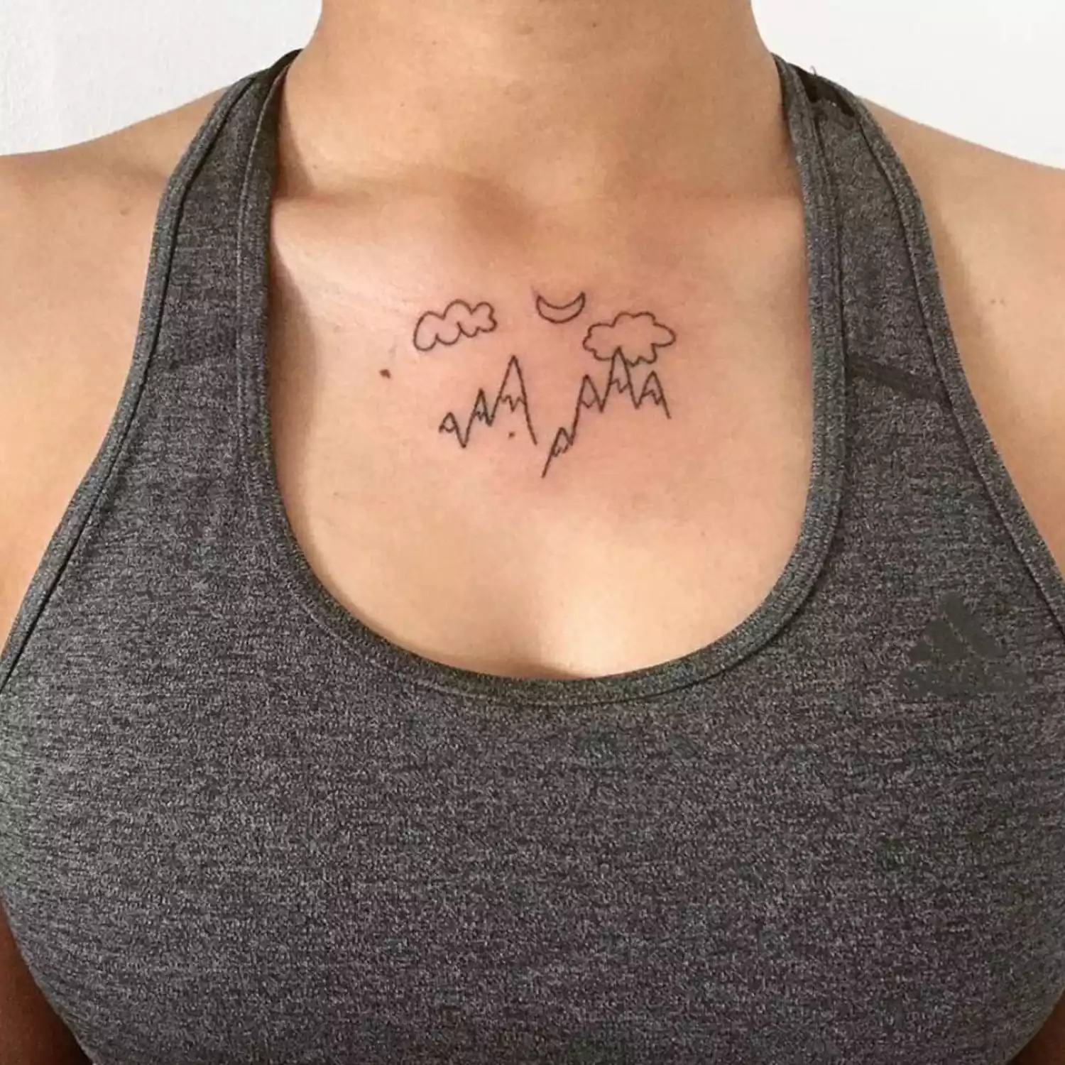 zoomed-in image of model with tattoo placement on center collarbone, with clouds, moon, and mountains in black ink