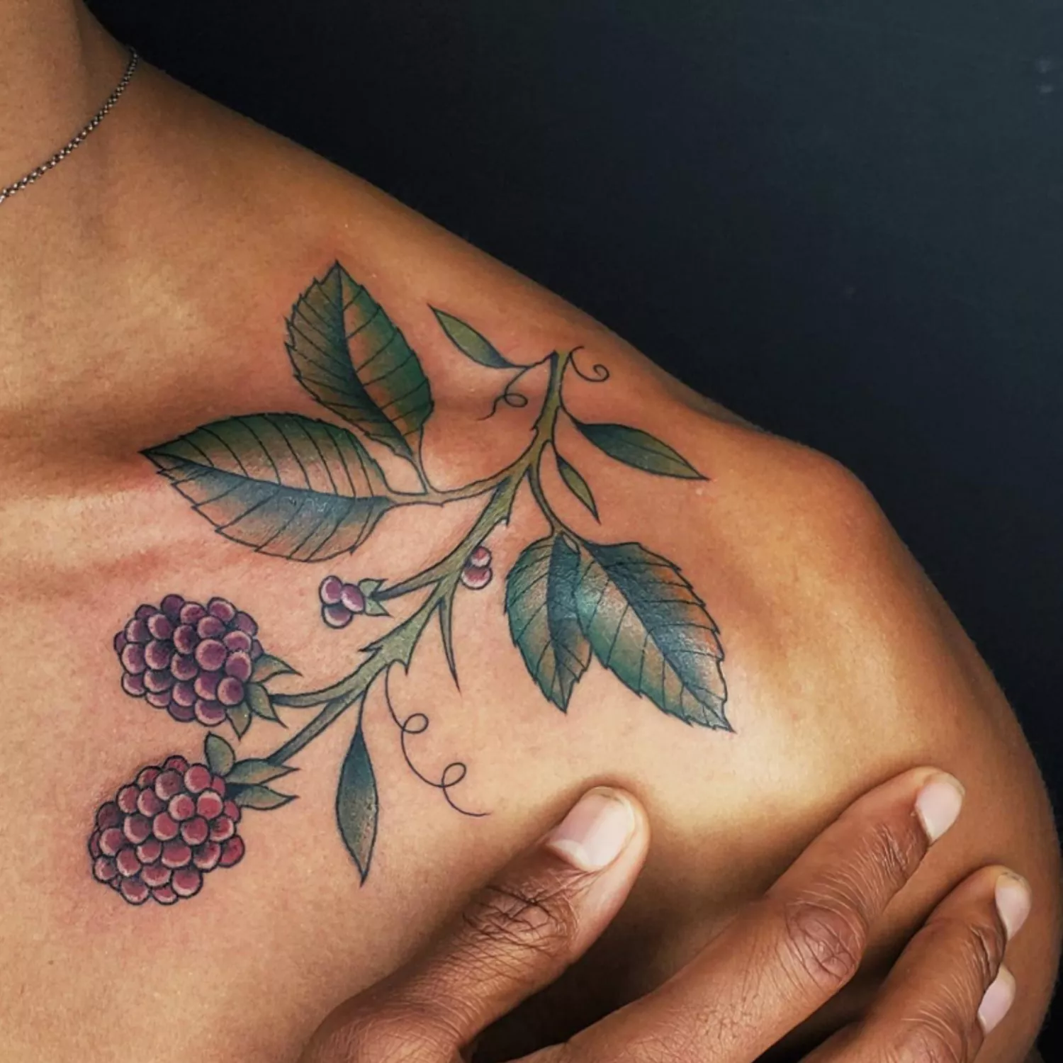 zoomed-in image of model with large tattoo going across collarbone, green leaves with purple berry bundles