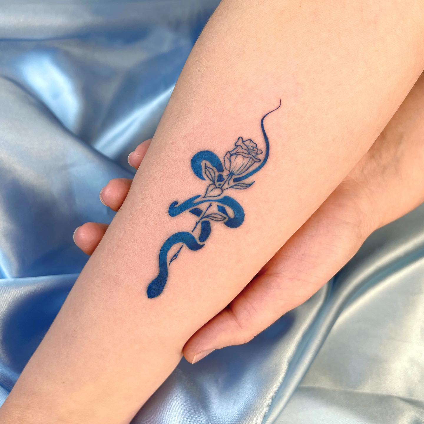 Rose and snake tattoo in blue ink located on the inner forearm