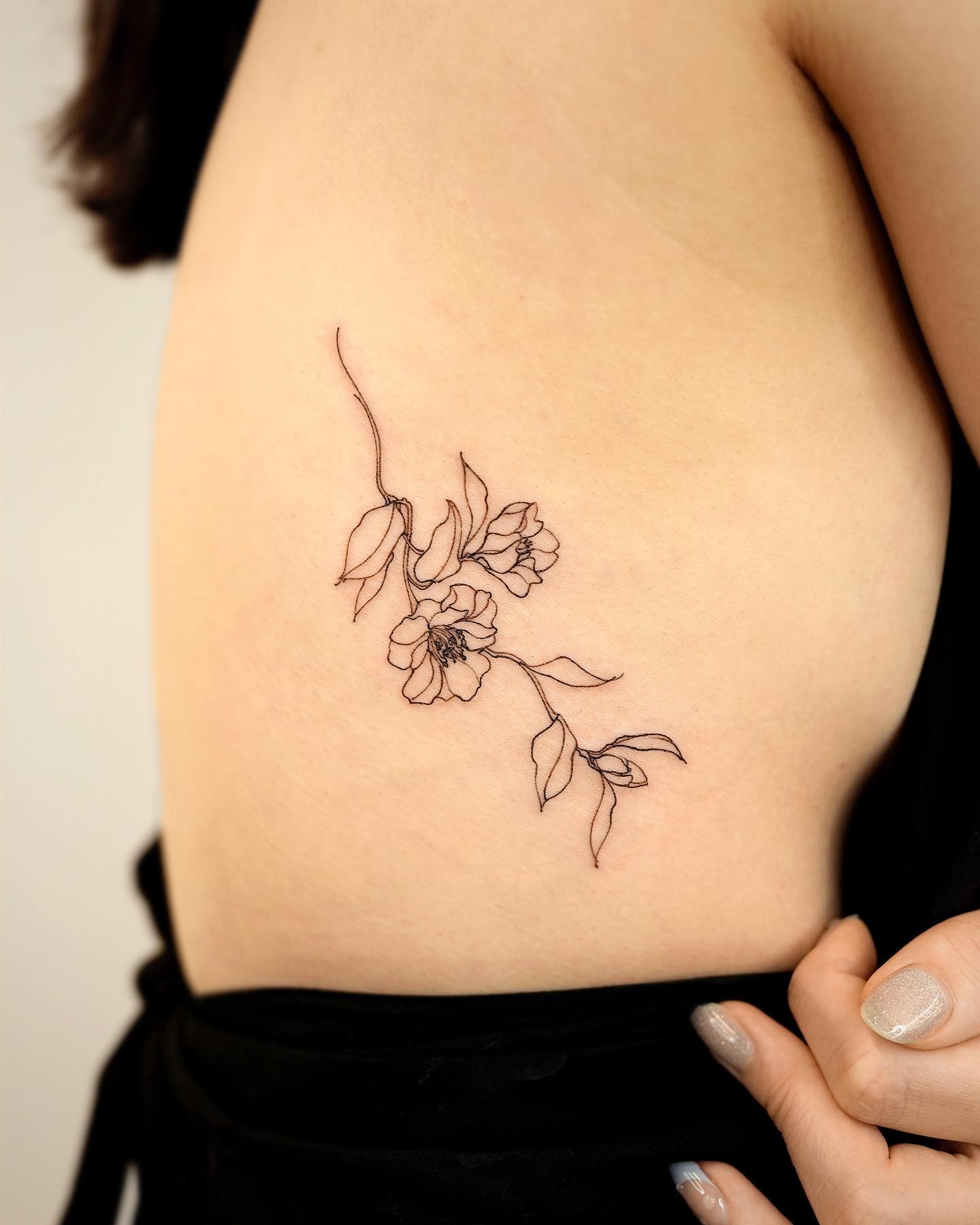 Camellia flower tattoo located on the sideboob, fine line style